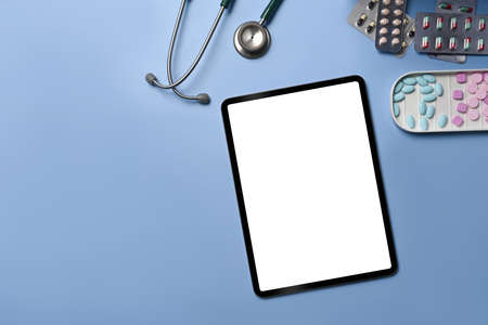 Digital tablet, stethoscope and colorful medical pills on blue background.の写真素材