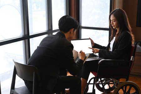 Businesswoman in wheelchair with colleagues in meeting room.の写真素材
