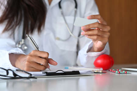 Cropped shot female doctor in white uniform writing medical information on documents.の写真素材