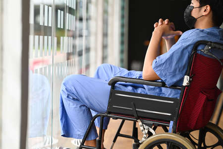 Pensive disabled patient on wheelchair alone at hospital and look through window.の写真素材