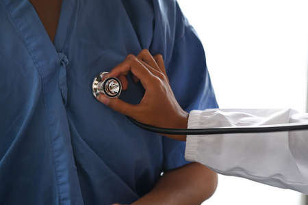 Cropped shot doctor holding stethoscope checking heart and lungs of male patient.の写真素材