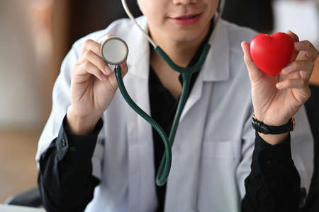 Smiling male doctor holding red heart and stethoscope. Health insurance concept.の写真素材