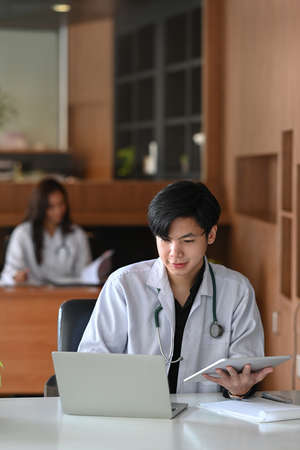 Male doctor in white uniform working with computer laptop in medical clinic office.の写真素材
