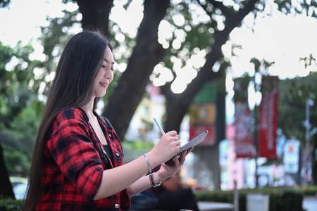 Smiling young woman sitting on bench in a city and using digital tablet.の写真素材