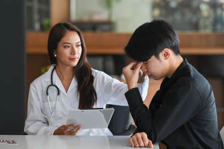 Depressed man consulting his health problem with female professional psychiatrist doctor.の写真素材