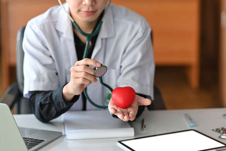 Doctor in white uniform holding red heart and stethoscope. Cardiology and insurance concept.の写真素材