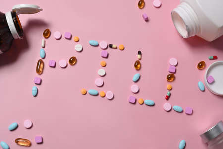 Colorful pills spilling out of a pill bottle on pink background.の写真素材