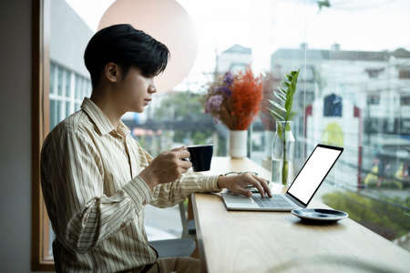 Smiling young Asian man sitting in bright office and reading book.の写真素材