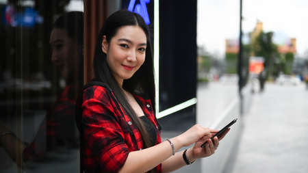 Portrait of young woman using smart phone while sitting on bench in city park.の写真素材