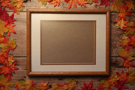 Vintage photo frame with autumn maple leaves on wooden background.の写真素材
