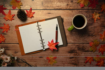 Above view empty notebook, coffee cup and autumn maple leaves on wooden background.の写真素材