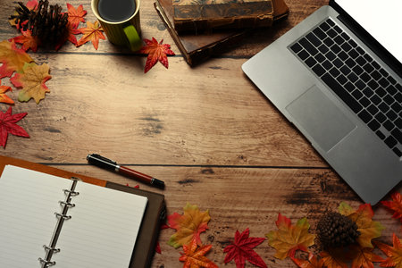 Laptop computer, coffee cup, notebook and autumn maple leaves on wooden table.の写真素材