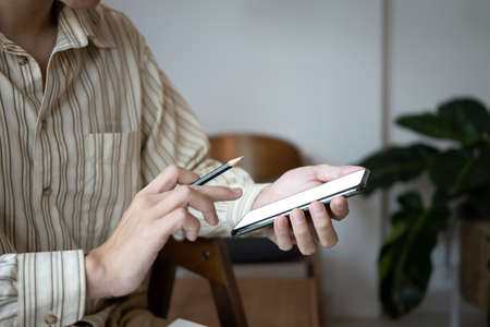 Cropped shot businessman holding pencil and using smart phone.の写真素材