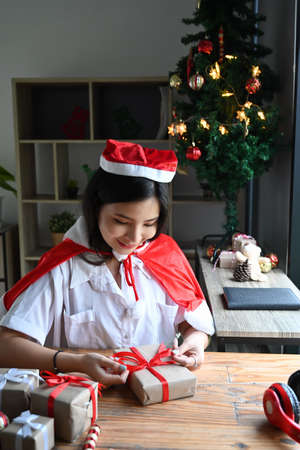 Smiling young woman in Santa hat looking at Christmas presents.の写真素材