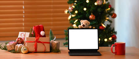 Computer tablet, cup of hot beverage and Christmas gift boxes on wooden table.の写真素材