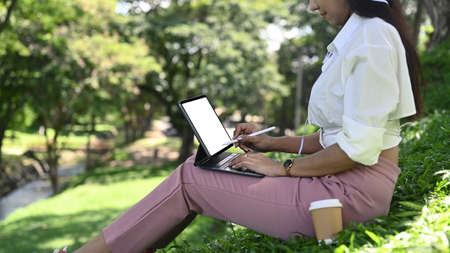 Young woman sitting in public park and working with computer tablet.の写真素材