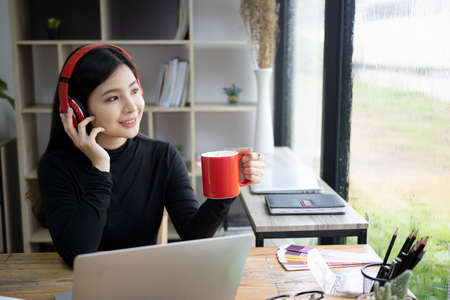 Happy young woman  listening to music in headphone and drinking hot coffee.の写真素材