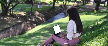 Young woman sitting in public park and working with computer tablet.の写真素材