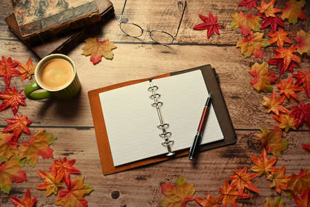 Empty notebook, pen, cup of hot coffee, glasses and maple leaves on wooden table.の写真素材