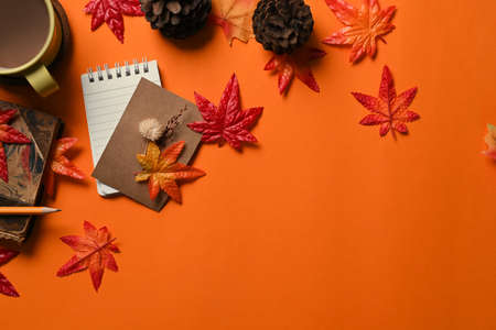 Top view notebook, coffee cup, pine cone and maple leaves on orange background.の写真素材