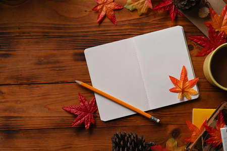 Top view notebook, cup of coffee, pine cone and maple leaves on orange background.の写真素材