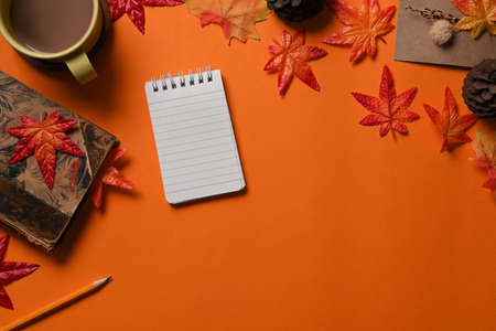 Top view notebook, cup of coffee, pine cone and maple leaves on orange background.の写真素材