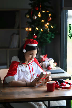 Cropped shot young woman opening Christmas gift box on wooden table.