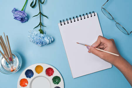 Overhead view woman holding paint brush and painting on notebook.の写真素材