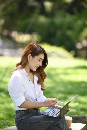 Beautiful woman sitting on bench in the city park and working with computer tablet.の写真素材