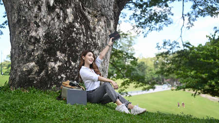 Beautiful woman sitting on bench in the city park and working with computer tablet.