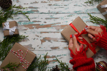 Above view woman in red sweater holding Christmas gift boxes on wooden background.