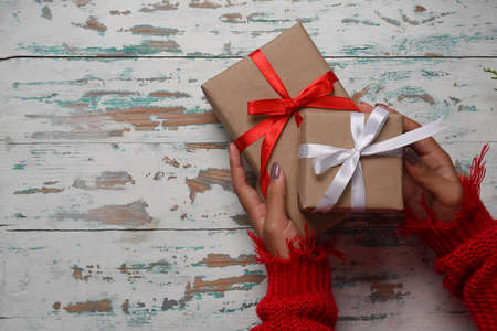 Above view woman in red sweater holding Christmas gift boxes on wooden background.