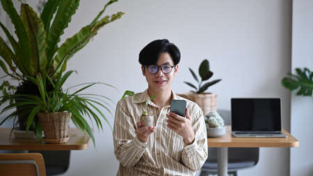 Handsome man small business entrepreneur holding potted plant and smiling to camera.の写真素材