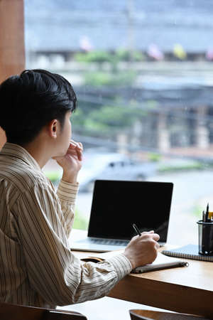 Side view man freelancer sitting near window and working with laptop computer.の写真素材