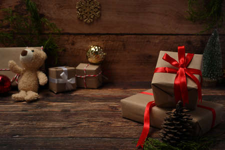 Christmas gift boxes with red ribbon, teddy bear, pine cones and fir branches on wooden table.の写真素材