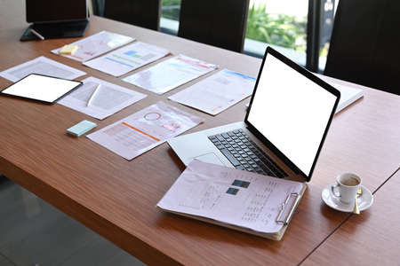 Laptop computer, coffee cup and financial documents on wooden table in office.の写真素材