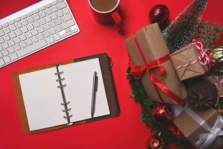 Christmas presents with red ribbon, pine cone, notebook and cup of coffee on red background.の写真素材