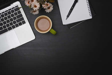 Laptop computer, empty notebook and coffee cup on black table.