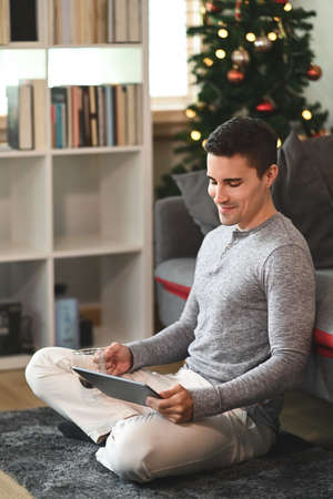 Young man sitting in living room and using digital tablet.