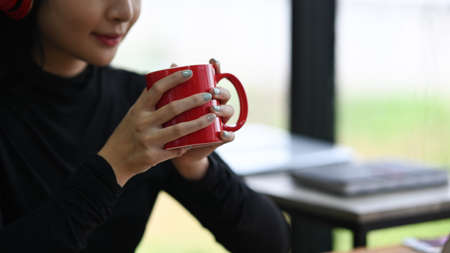 Cropped shot young woman holding red cup of hot coffee.の写真素材