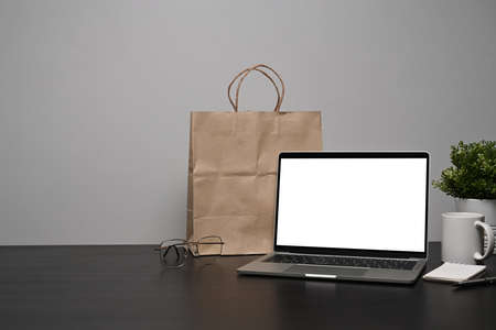 Mock up laptop computer, paper bag, coffee cup and houseplant on black table.の写真素材