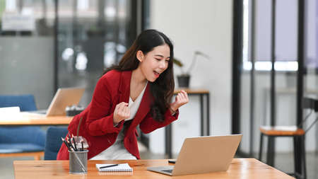 Happy businesswoman standing at her workplace and celebrating successful project.