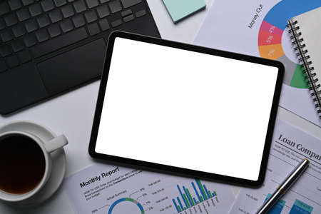 Above view mock up digital tablet, coffee cup and financial documents on white office desk.