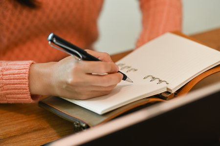 Close up view young woman in warm sweater making notes to her diary.
