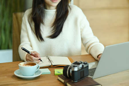 Young woman sitting in front of laptop computer and checking social media on her smart phone.