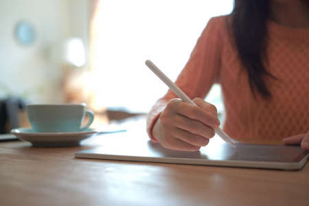 Young woman sitting in front of laptop computer and checking social media on her smart phone.の写真素材