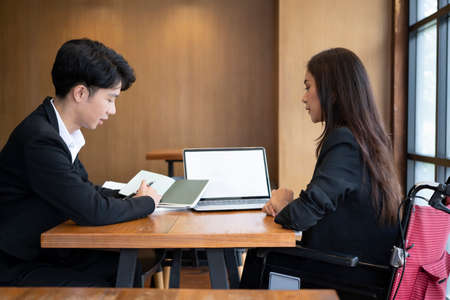 Businesswoman with disability analyzing financial on laptop computer with colleague in office.の写真素材