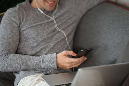 Cropped shot smiling man using smart phone and laptop computer on sofa.の写真素材