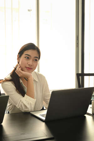 Portrait of thoughtful businesswoman sitting in office desk and working with laptop computer.の写真素材