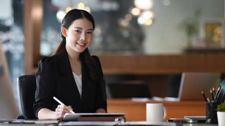 Attractive businesswoman sitting in her office room and smiling to camera.の写真素材